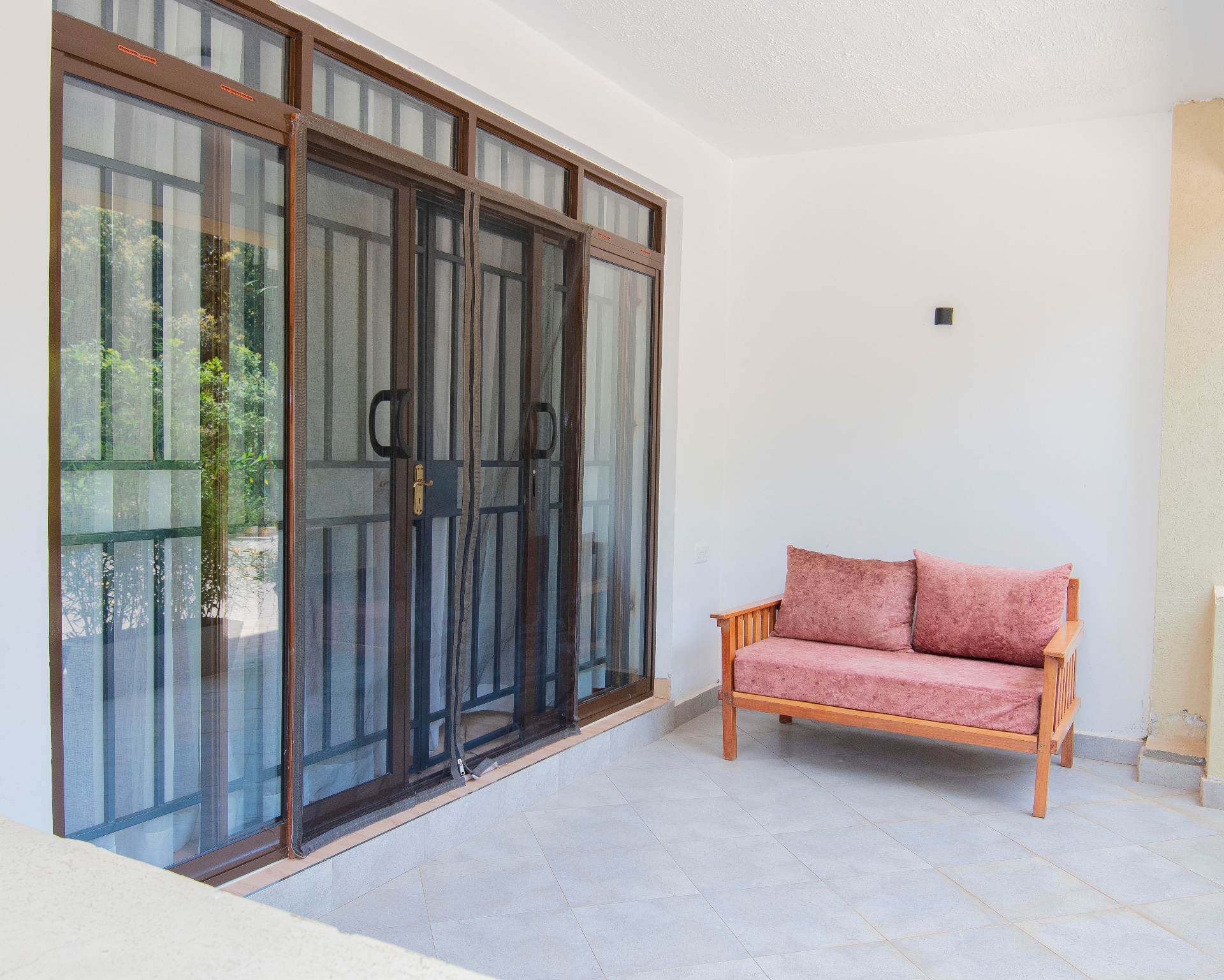 Veranda with wooden bench and glass doors overlooking lush greenery