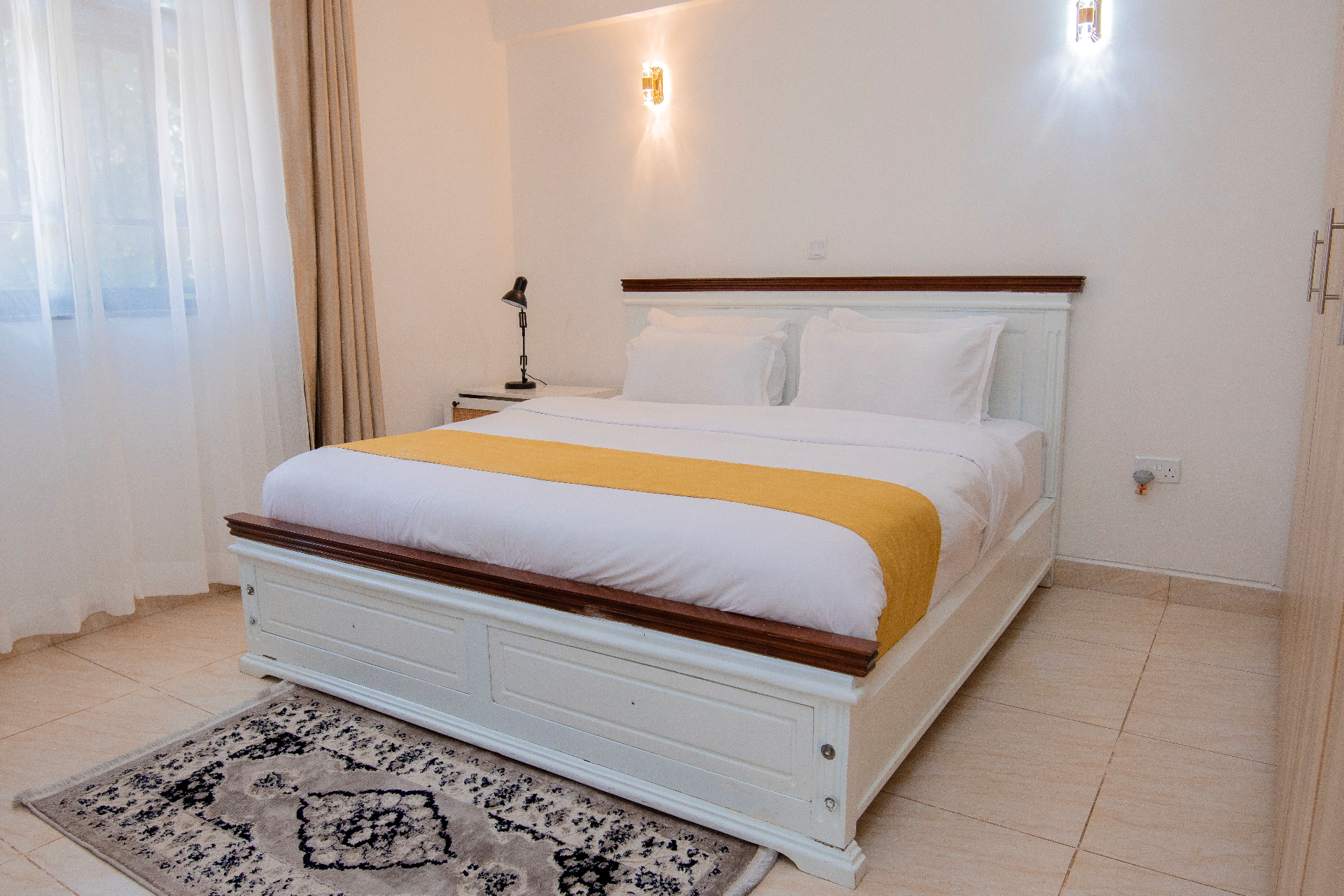 One-Bedroom Furnished – queen bed with yellow runner, bright window