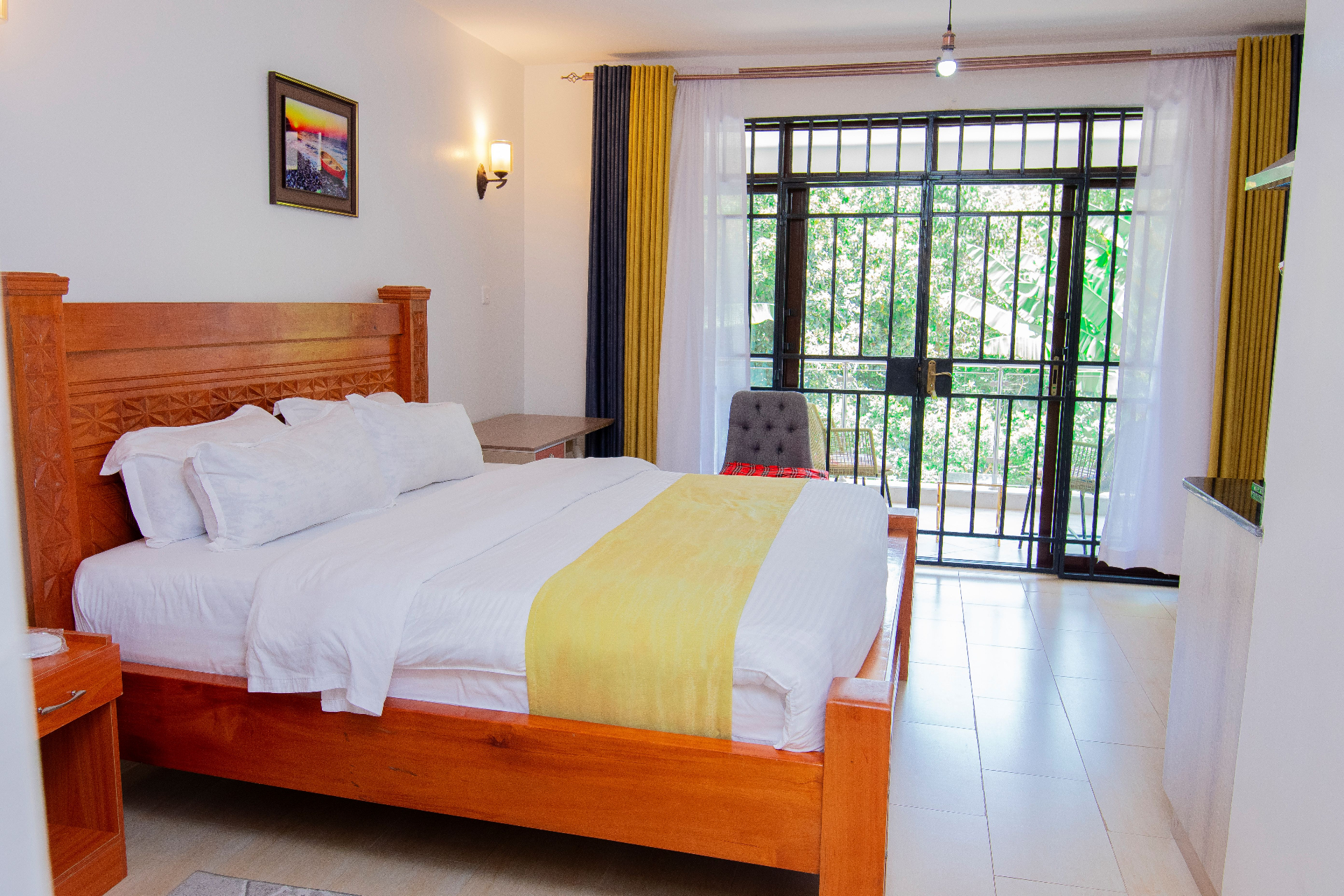 Deluxe Studio with Kitchenette – bedroom with carved wooden bed, balcony access