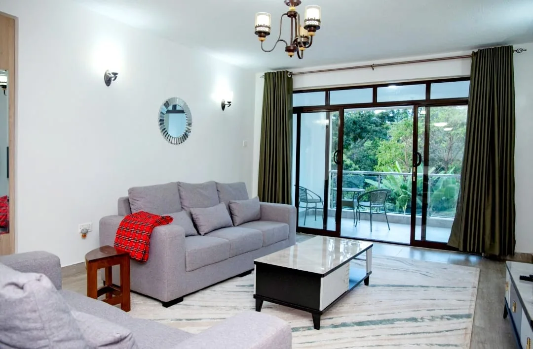 Two-Bedroom Furnished – bright living room with grey sofas, chandelier, and balcony doors